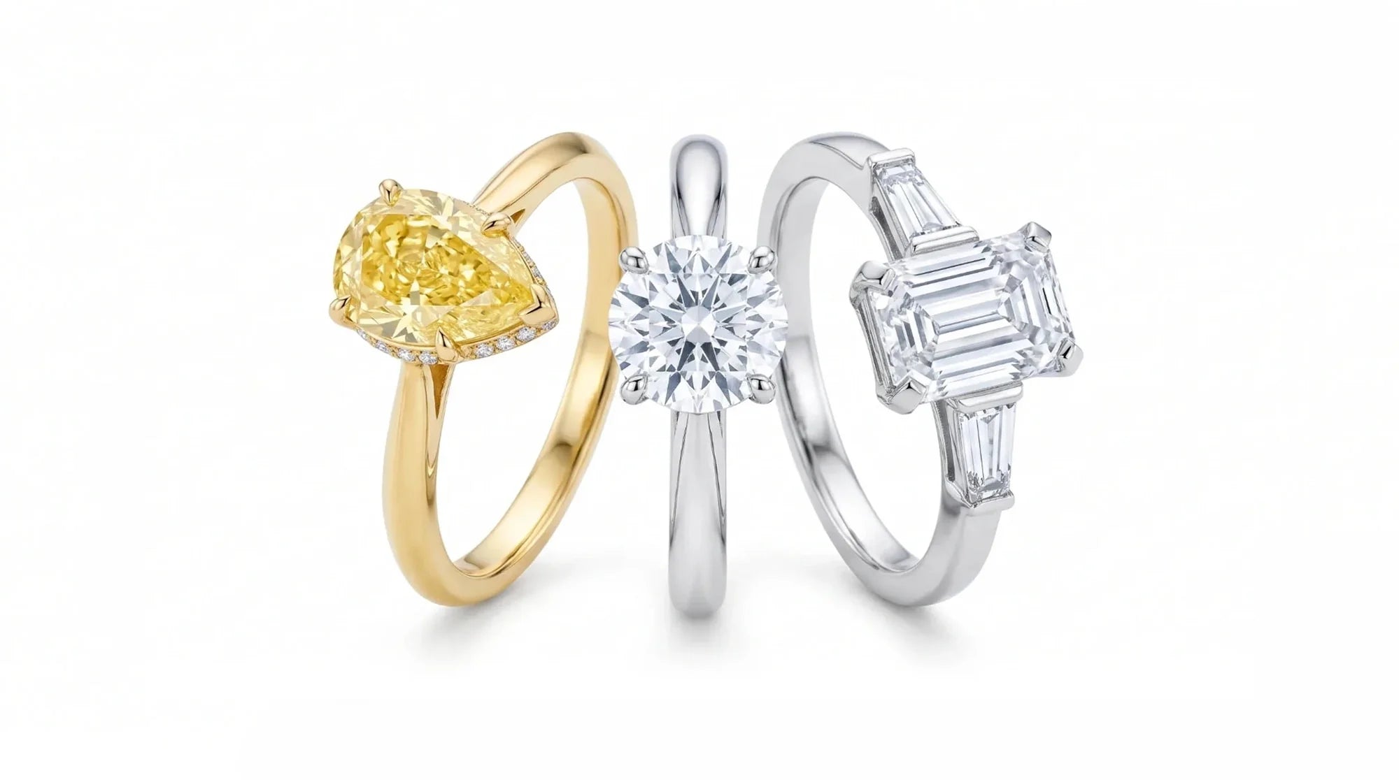 Tre solitari affiancati su fondo bianco: uno con diamante giallo a goccia in oro giallo, uno rotondo in oro bianco e uno con taglio smeraldo affiancato da due baguette