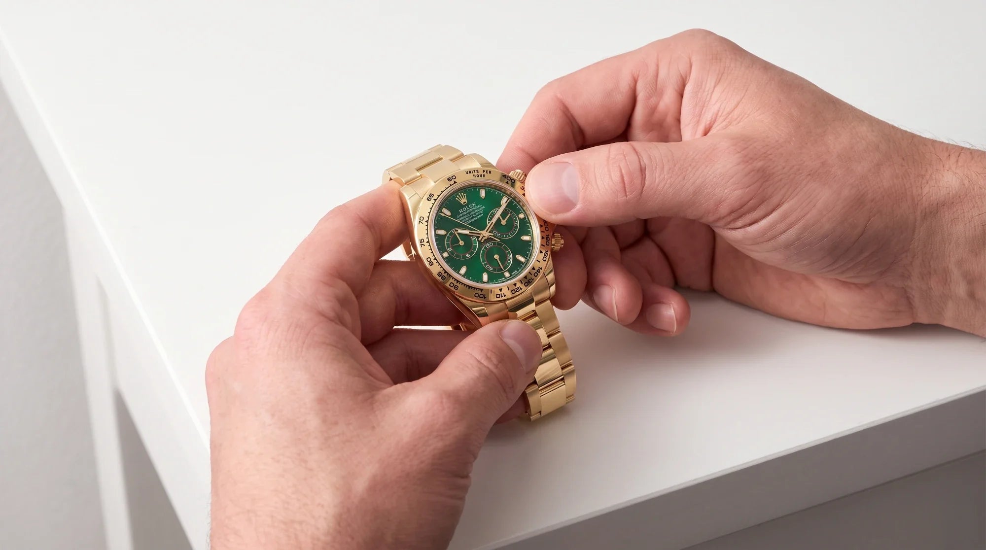 Un Rolex Daytona in oro giallo con quadrante verde fra le mani, appoggiato al banco